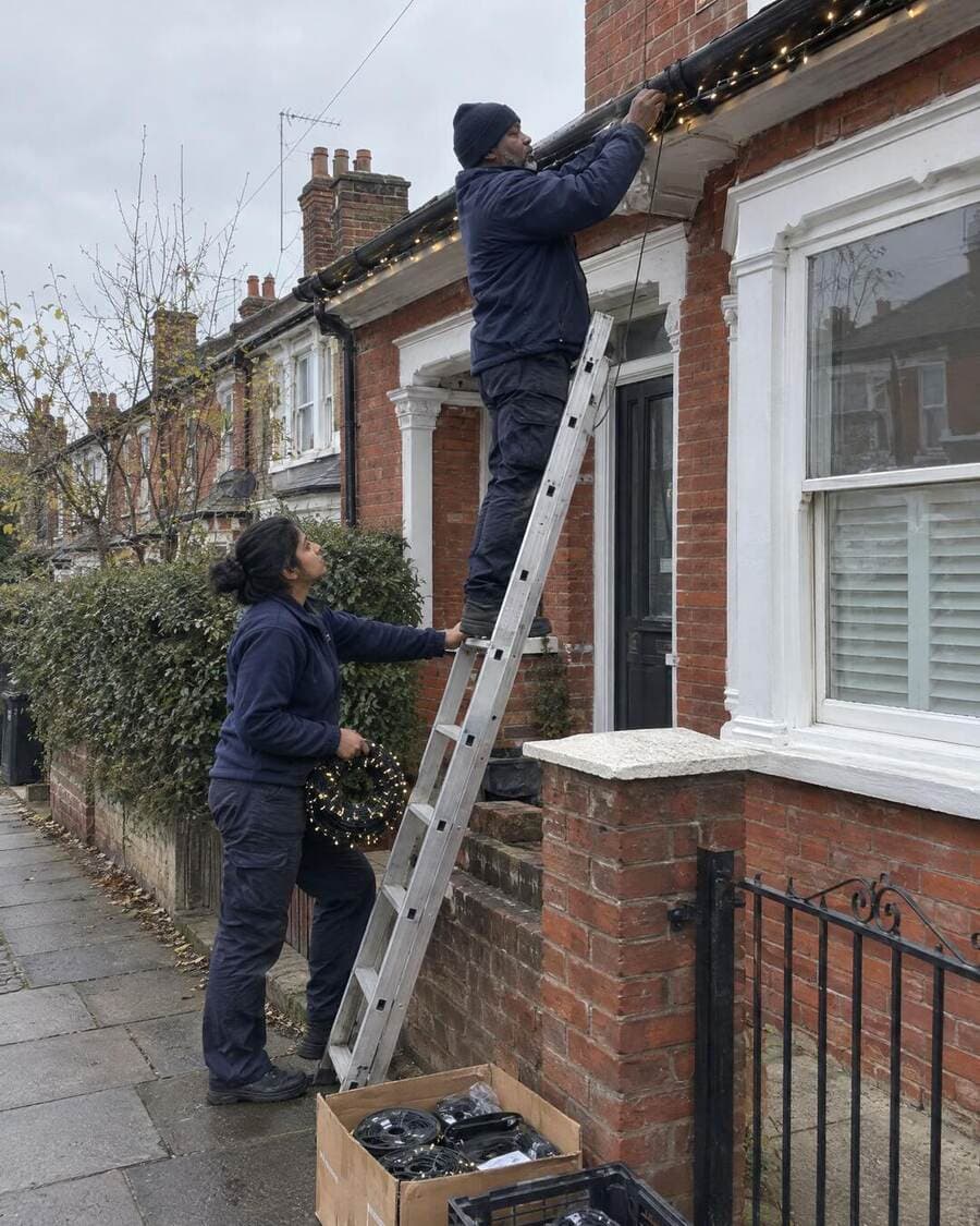 Installer on a ladder fitting warm-white Christmas lights to a London house