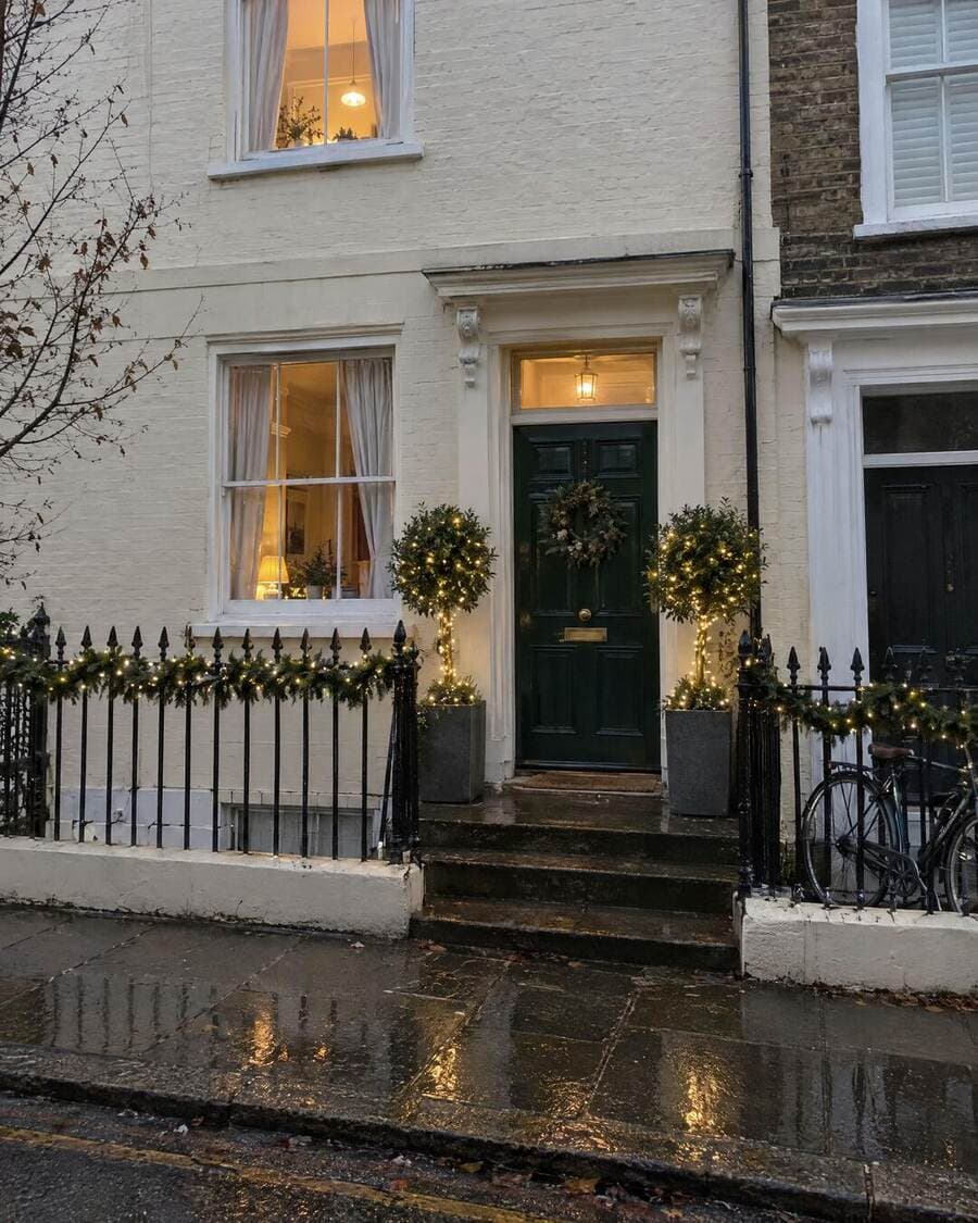 Lit Christmas garland and wreath around a London townhouse door with illuminated bay trees